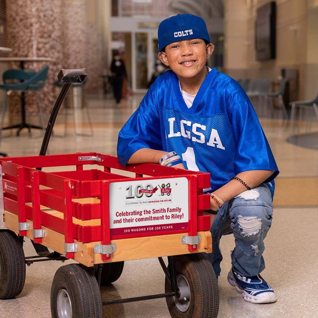 Riley kid boy next to Riley Red wagon with 100 year license plate