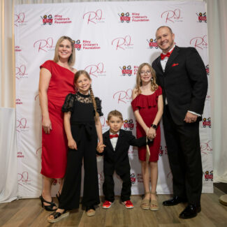 Riley family in front of backdrop with Riley logos at Red event