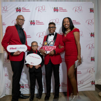 Riley family in front of backdrop with Riley logos at Riley Red event