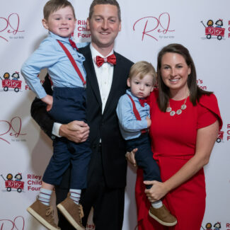 Riley family in front of backdrop with Riley logos at Riley Red event