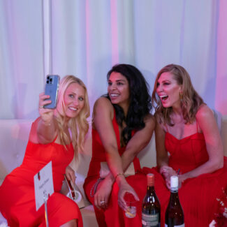 Women on couch wearing red dresses taking a selfie.