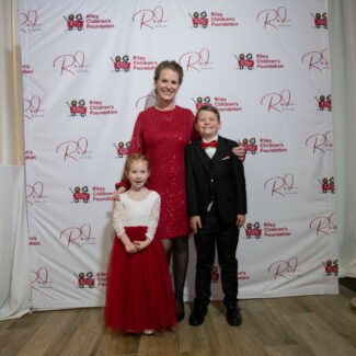 Riley family in front of backdrop with Riley logos at Riley Red event